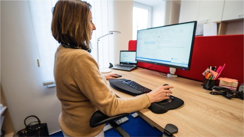 Žena sedící vzpřímeně u stolu s ergonomickým kancelářským vybavením