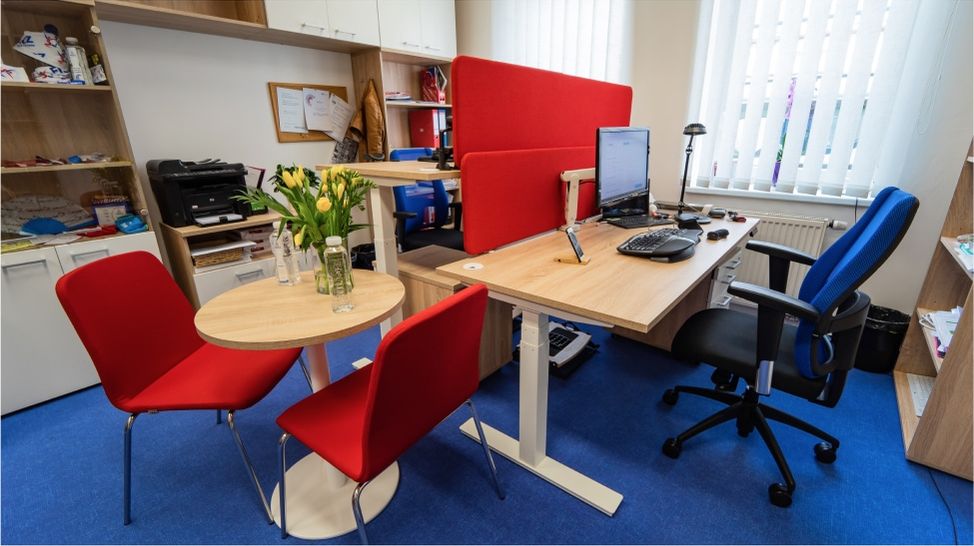 Pohled na ergonomicky vybavenou kancelář s červenými a modrými prvky